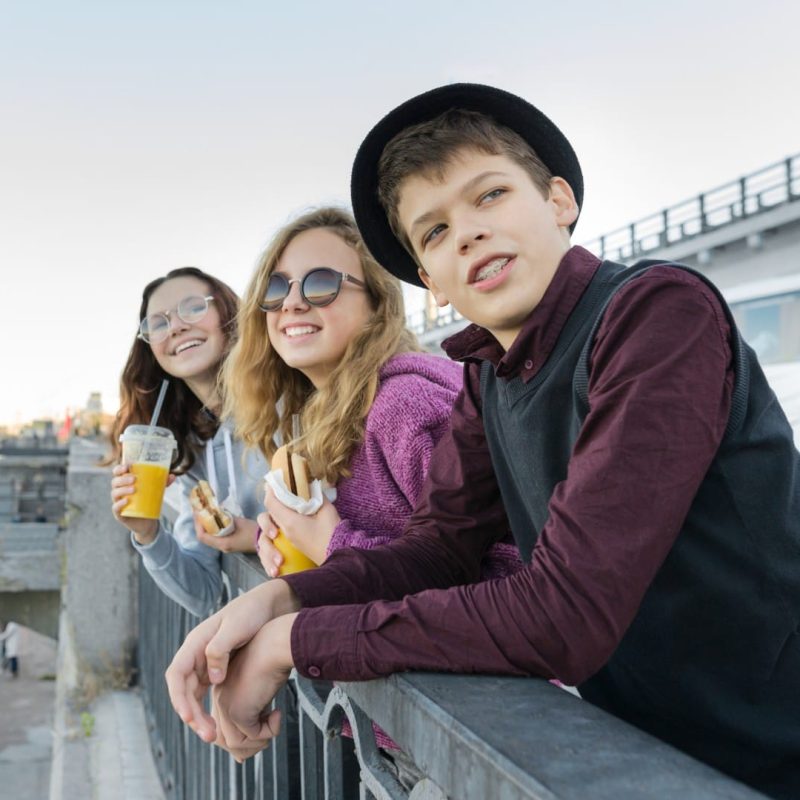 Teenagers boy and two girls with street food talking outdoor.